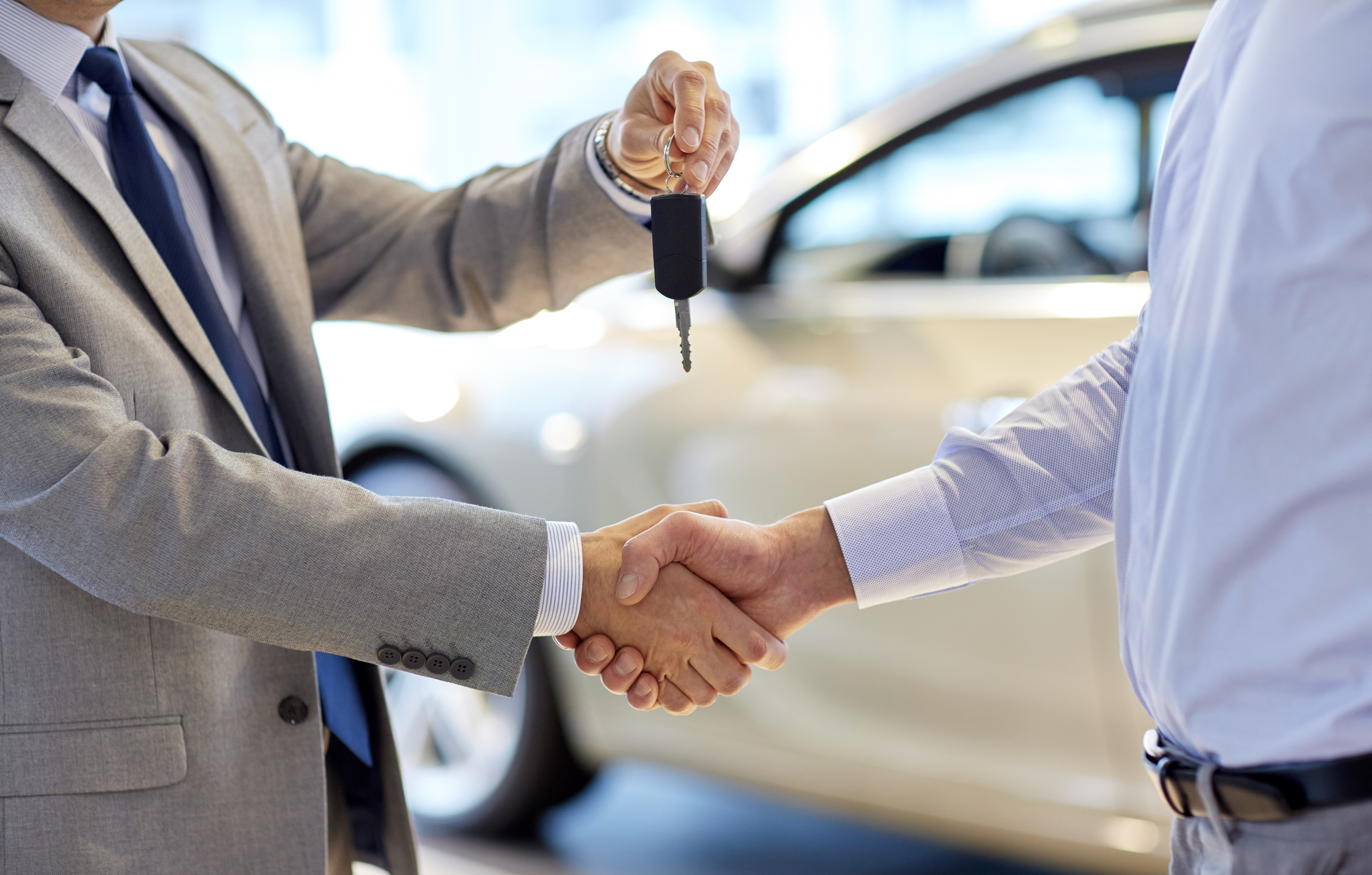 auto business, car sale, deal, gesture and people concept - close up of dealer giving key to new owner and shaking hands in auto show or salon